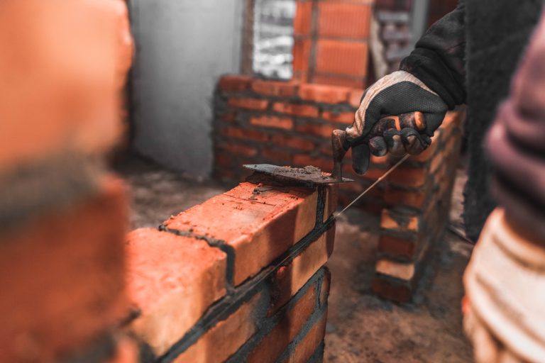 Bricklayer puts bricks to make a wall